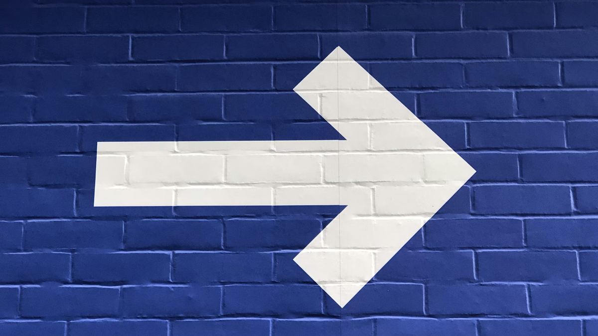 Conceptual image: a large white arrow painted on a blue brick wall points right - illustrating an obvious and clear direction.